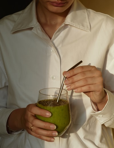 穿着白色纽扣衬衫的人，手里拿着绿色液体的透明酒杯
